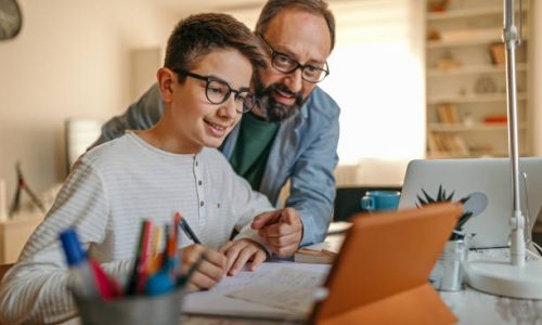 Father embracing son from behind while helping him with homework