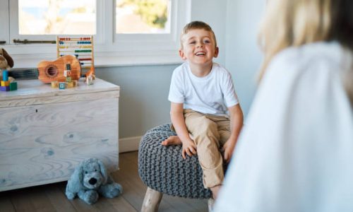 An adorable little boy sitting on a chair while talking to a caucasian therapist. Cute little boy talking to a psychologist. Child checking in with a counsellor at a foster home before being adopted